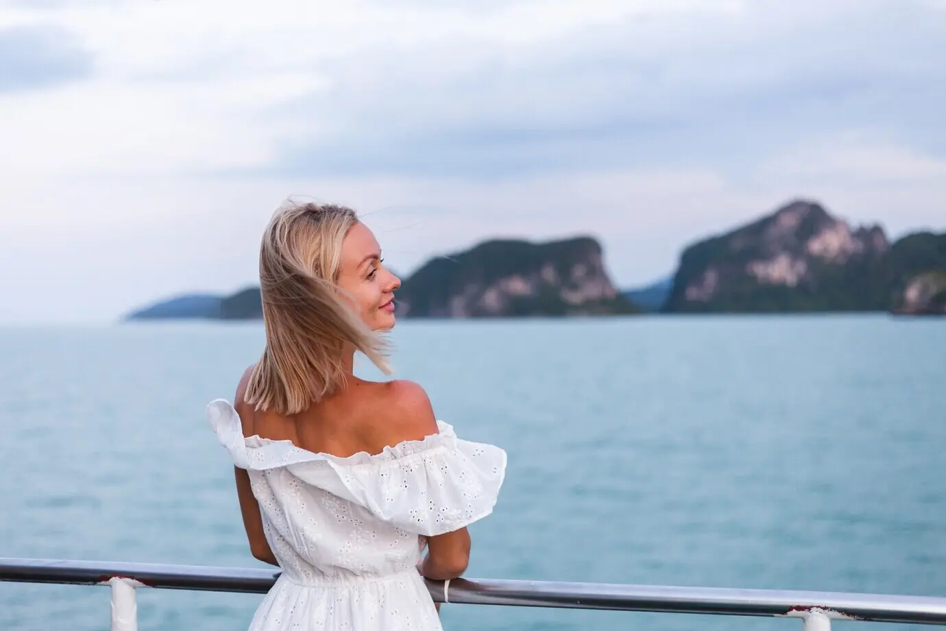 A romantic portrait of a woman in a white dress sailing on a large ferry boat.